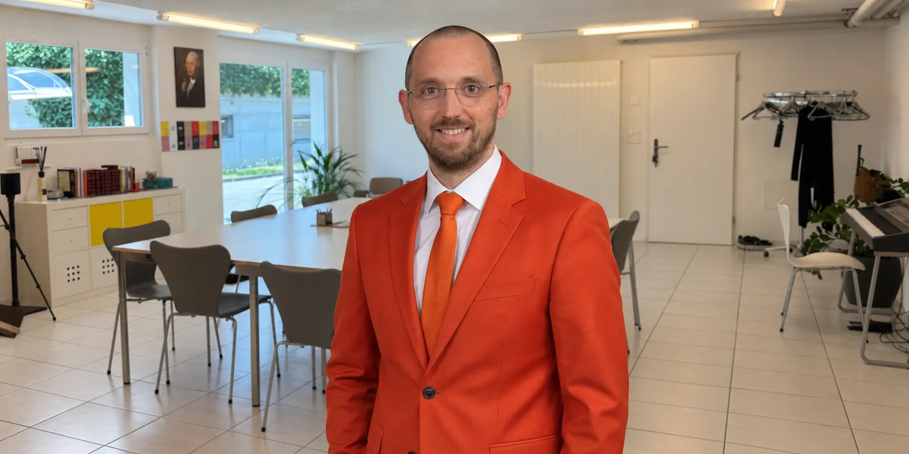 Andreas Hosang im orangefarbenen Anzug in einem hellen Besprechungsraum, mit Blick in die Kamera.